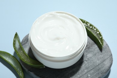 Moisturizing cream with extract of aloe vera and cut leaves on light blue background, closeup