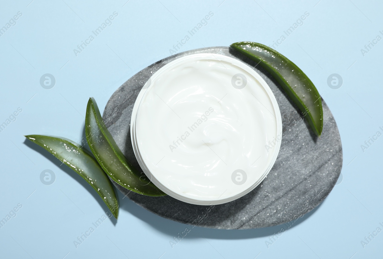 Photo of Moisturizing cream with extract of aloe vera and cut leaves on light blue background, flat lay