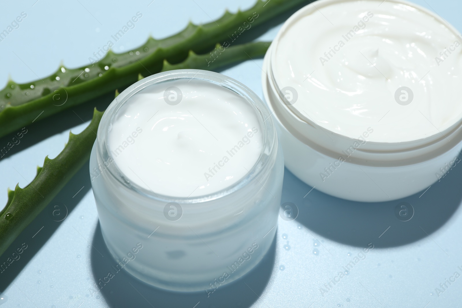 Photo of Moisturizing cream with extract of aloe vera, cut leaves and water drops on light blue background, closeup