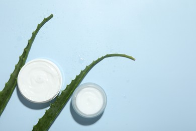 Moisturizing cream with extract of aloe vera, cut leaves and water drops on light blue background, flat lay. Space for text