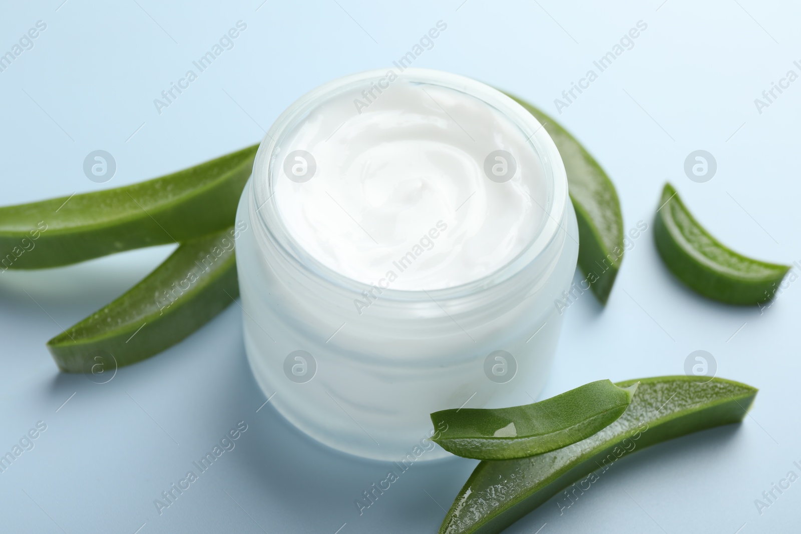 Photo of Moisturizing cream with extract of aloe vera and cut leaves on light blue background, closeup