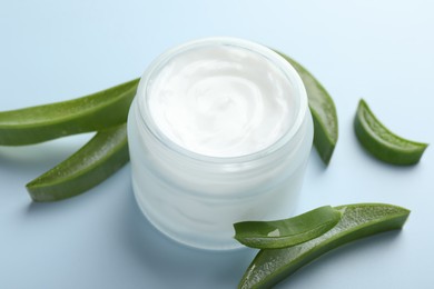 Photo of Moisturizing cream with extract of aloe vera and cut leaves on light blue background, closeup