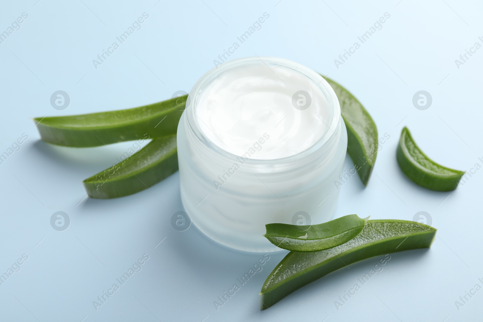 Photo of Moisturizing cream with extract of aloe vera and cut leaves on light blue background, closeup