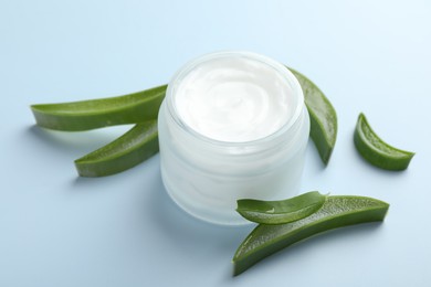 Moisturizing cream with extract of aloe vera and cut leaves on light blue background, closeup