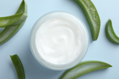 Moisturizing cream with extract of aloe vera and cut leaves on light blue background, flat lay