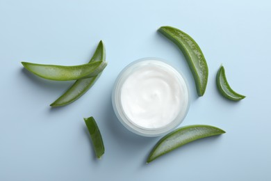 Moisturizing cream with extract of aloe vera and cut leaves on light blue background, flat lay