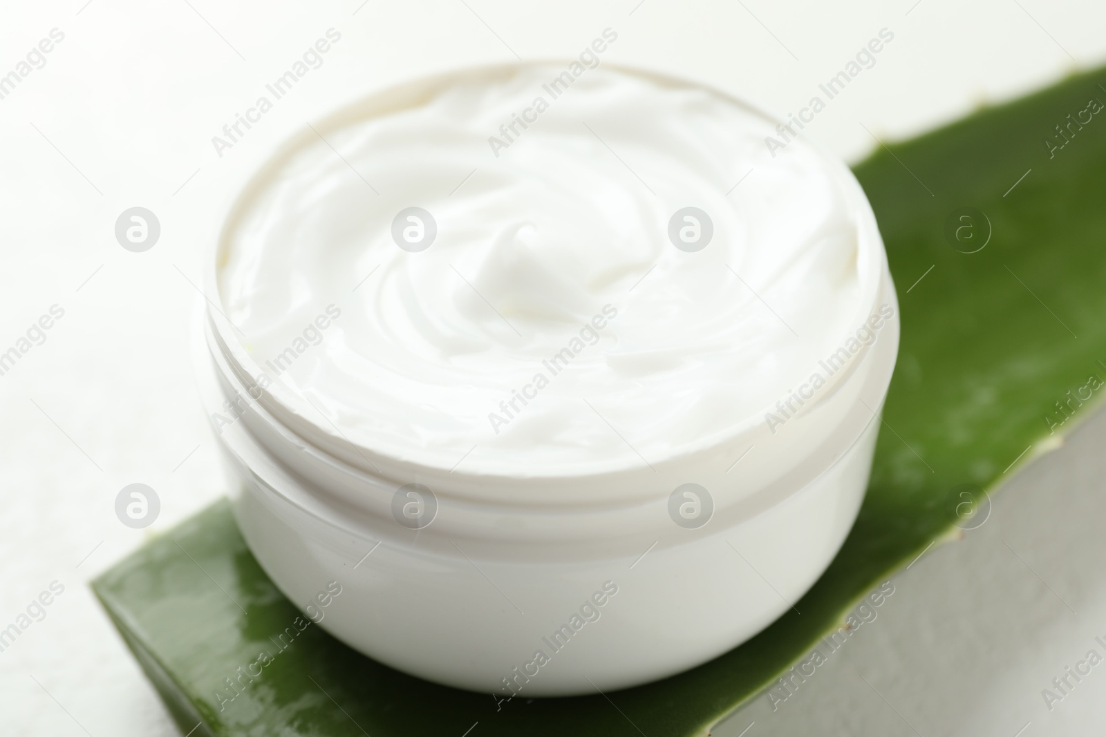 Photo of Moisturizing cream with extract of aloe vera and cut leaf on white background, closeup