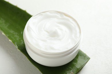 Moisturizing cream with extract of aloe vera and cut leaf on white textured background, closeup