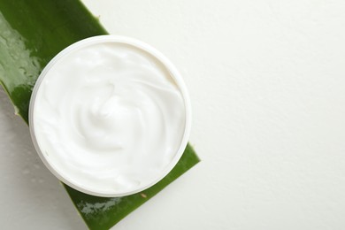 Photo of Moisturizing cream with extract of aloe vera and cut leaf on white background, top view. Space for text