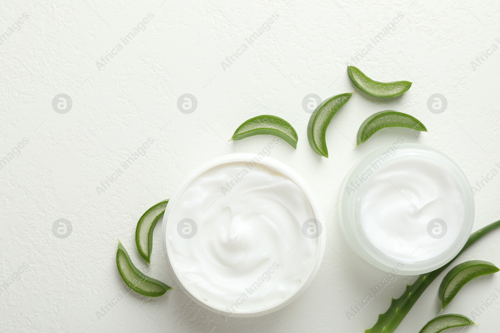 Photo of Moisturizing cream with extract of aloe vera and cut leaves on white textured background, flat lay. Space for text