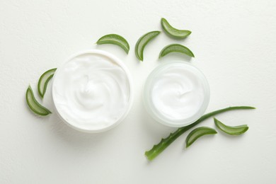 Photo of Moisturizing cream with extract of aloe vera and cut leaves on white textured background, flat lay