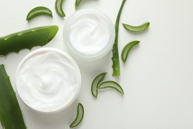 Photo of Moisturizing cream with extract of aloe vera and cut leaves on white textured background, flat lay