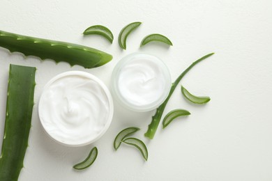 Photo of Moisturizing cream with extract of aloe vera and cut leaves on white textured background, flat lay