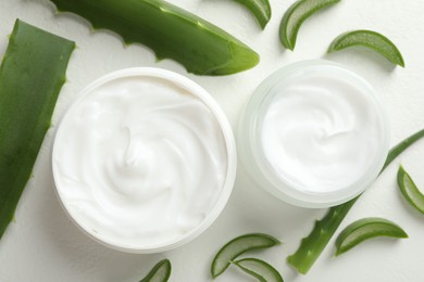 Photo of Moisturizing cream with extract of aloe vera and cut leaves on white textured background, flat lay