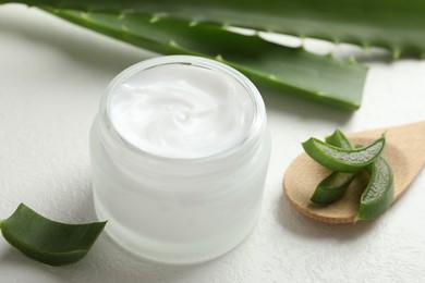 Photo of Moisturizing cream with extract of aloe vera and cut leaves on white textured background, closeup