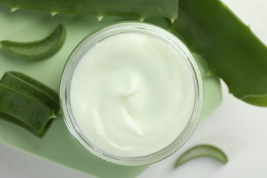 Photo of Moisturizing cream with extract of aloe vera and cut leaves on white background, flat lay