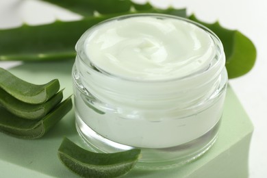 Photo of Moisturizing cream with extract of aloe vera, cut leaves and podium on white background, closeup