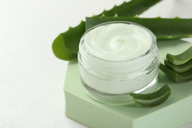 Photo of Moisturizing cream with extract of aloe vera, cut leaves and podium on white background, closeup. Space for text