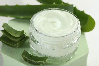 Photo of Moisturizing cream with extract of aloe vera, cut leaves and podium on white background, closeup