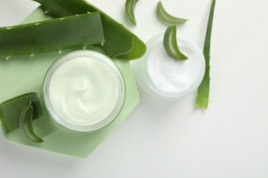 Photo of Moisturizing cream with extract of aloe vera and cut leaves on white background, flat lay. Space for text