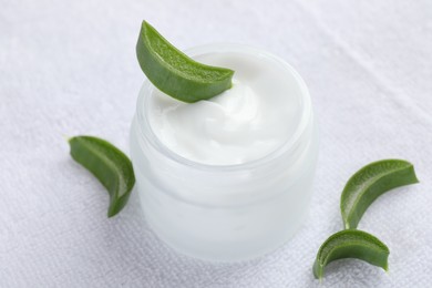 Photo of Moisturizing cream with extract of aloe vera and cut leaves on white towel, closeup