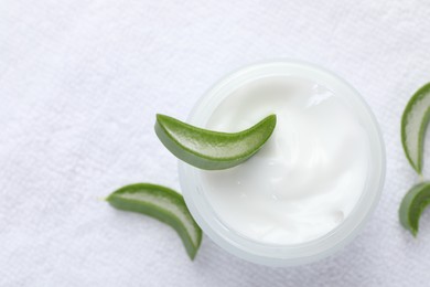 Photo of Moisturizing cream with extract of aloe vera and cut leaves on white towel, top view