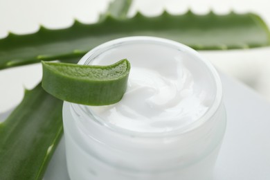 Photo of Moisturizing cream with extract of aloe vera and cut leaves on white background, closeup