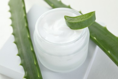 Photo of Moisturizing cream with extract of aloe vera and cut leaves on white background, closeup