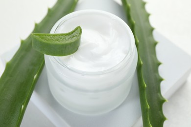 Photo of Moisturizing cream with extract of aloe vera and cut leaves on white background, closeup