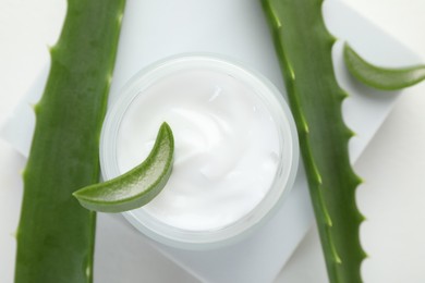 Photo of Moisturizing cream with extract of aloe vera and cut leaves on white background, flat lay