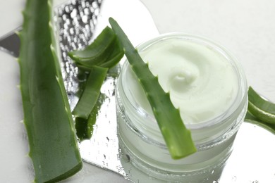 Photo of Moisturizing cream with extract of aloe vera, cut leaves and wet mirror on white background, closeup