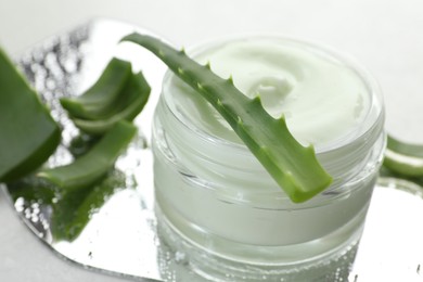 Photo of Moisturizing cream with extract of aloe vera, cut leaves and wet mirror on white background, closeup