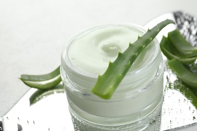 Photo of Moisturizing cream with extract of aloe vera, cut leaves and wet mirror on white background, closeup