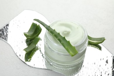 Photo of Moisturizing cream with extract of aloe vera, cut leaves and wet mirror on white background, closeup