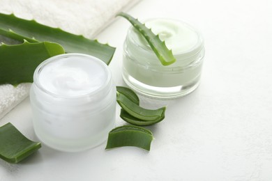 Photo of Moisturizing cream with extract of aloe vera, cut leaves and towel on white textured background, closeup