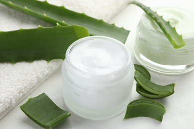 Photo of Moisturizing cream with extract of aloe vera, cut leaves and towel on white textured background, closeup