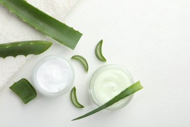 Photo of Moisturizing cream with extract of aloe vera, cut leaves and towel on white textured background, flat lay