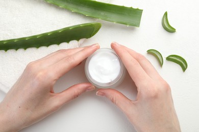 Photo of Woman with moisturizing cream, aloe vera leaves and towel at white textured table, top view