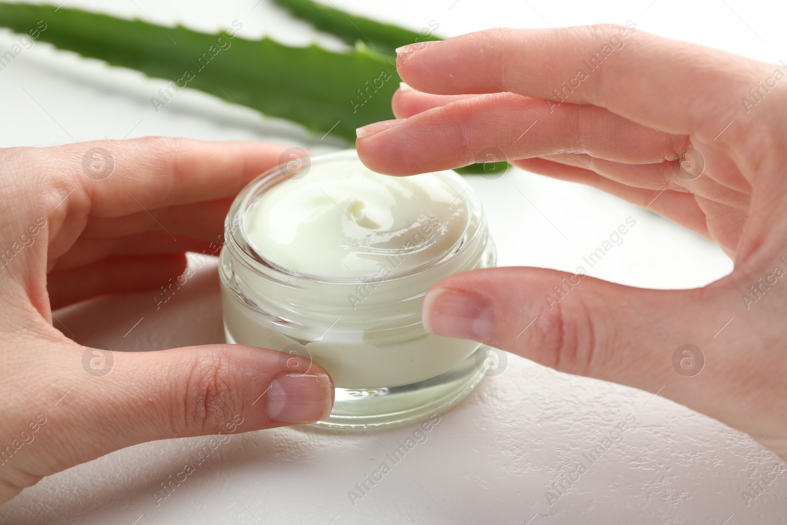 Photo of Woman with moisturizing cream and aloe vera leaves at white textured table, closeup