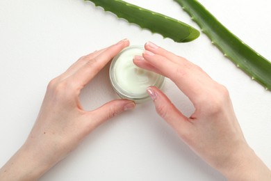 Photo of Woman with moisturizing cream and aloe vera leaves at white textured table, top view