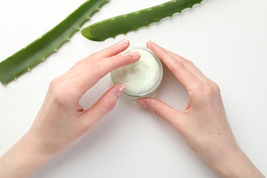 Photo of Woman with moisturizing cream and aloe vera leaves at white textured table, top view