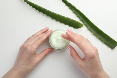 Photo of Woman with moisturizing cream and aloe vera leaves at white textured table, top view