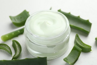 Photo of Moisturizing cream with extract of aloe vera and cut leaves on white textured background, closeup