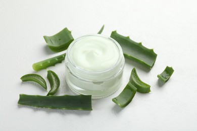 Photo of Moisturizing cream with extract of aloe vera and cut leaves on white textured background, closeup