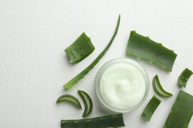 Photo of Moisturizing cream with extract of aloe vera and cut leaves on white textured background, flat lay. Space for text