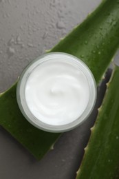 Photo of Moisturizing cream with extract of aloe vera in jar, cut leaves and water drops on grey background, flat lay