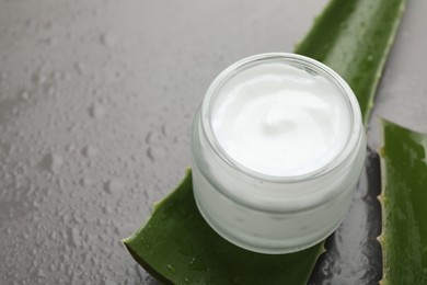 Photo of Moisturizing cream with extract of aloe vera in jar, cut leaves and water drops on grey background, closeup. Space for text