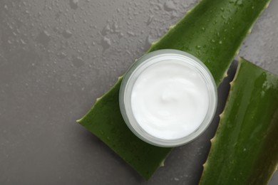 Photo of Moisturizing cream with extract of aloe vera in jar, cut leaves and water drops on grey background, flat lay. Space for text