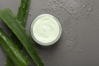 Photo of Moisturizing cream with extract of aloe vera in jar, cut leaves and water drops on grey background, flat lay. Space for text