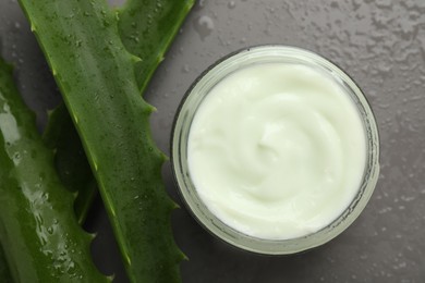 Photo of Moisturizing cream with extract of aloe vera in jar, cut leaves and water drops on grey background, flat lay